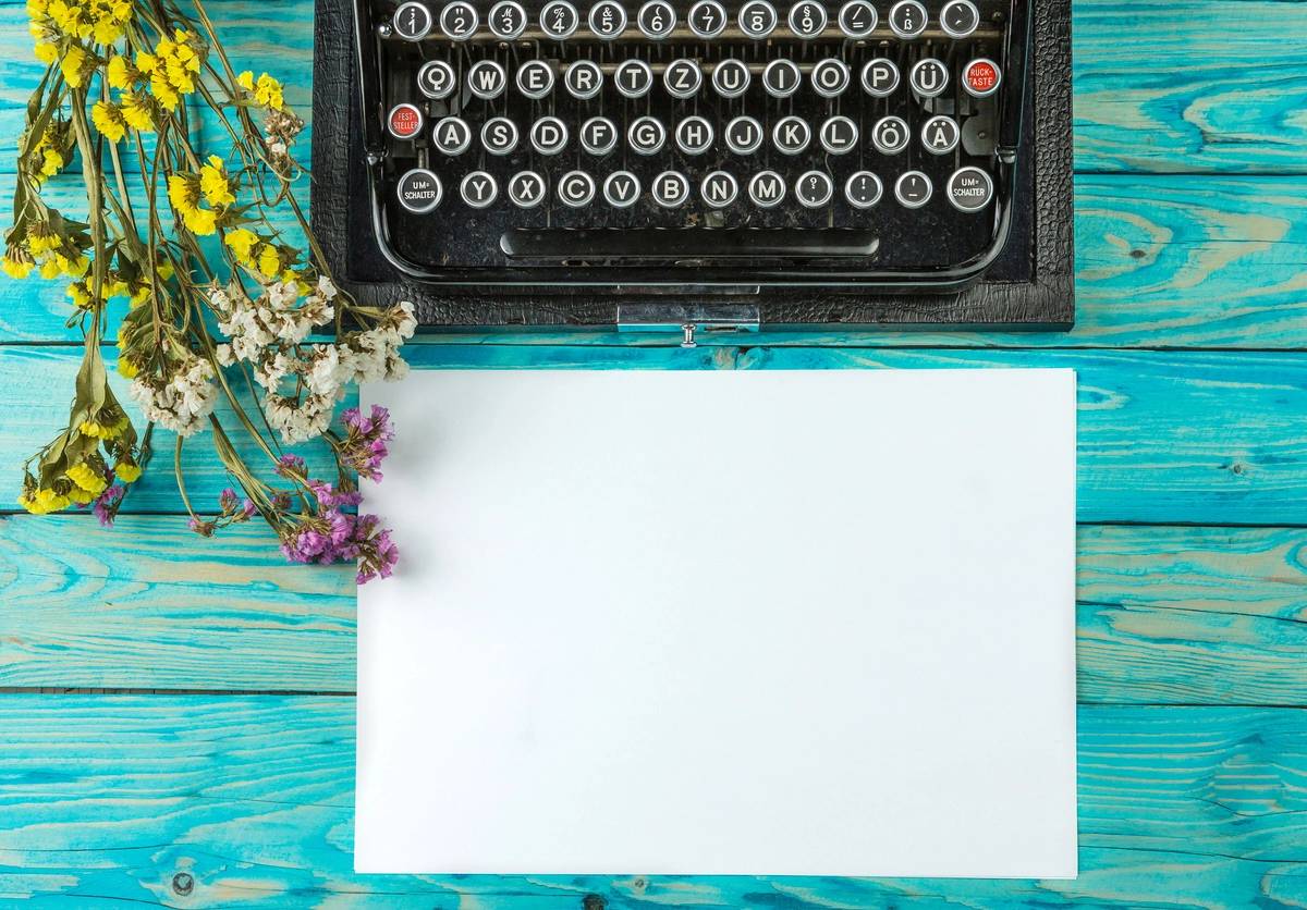 A typewriter with paper and flowers on the table.