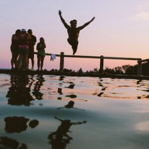 A group of people standing around water and one person jumping in the air.