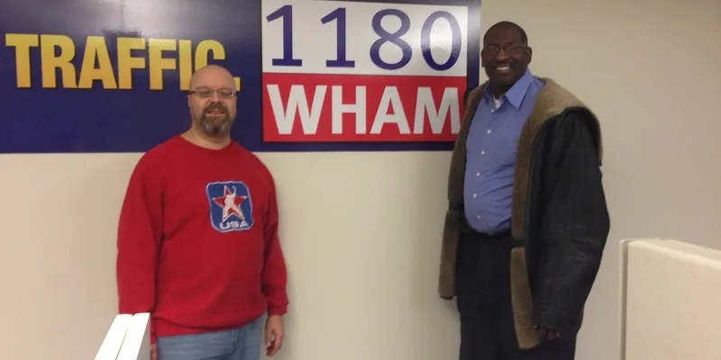 Two men standing by a WHAM sign.